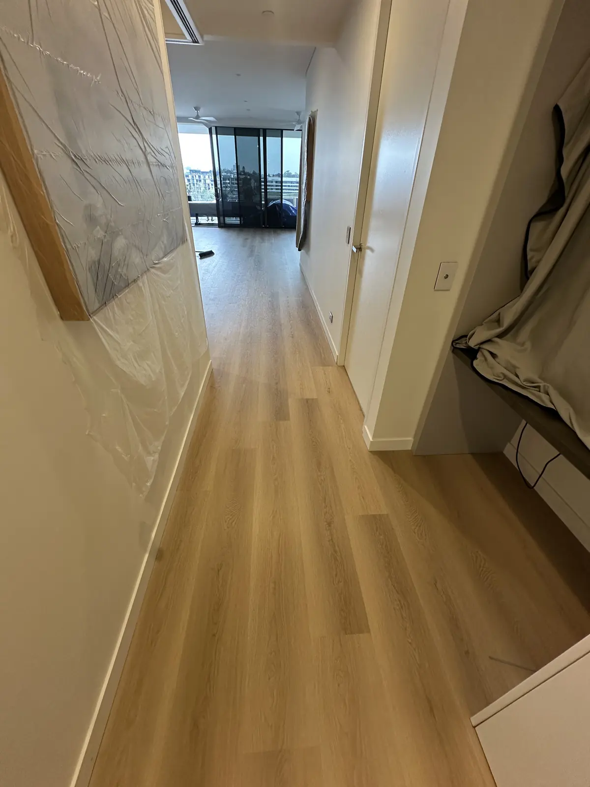 Finished plank flooring running down a Toowong apartment hallway with artwork wrapped for protection