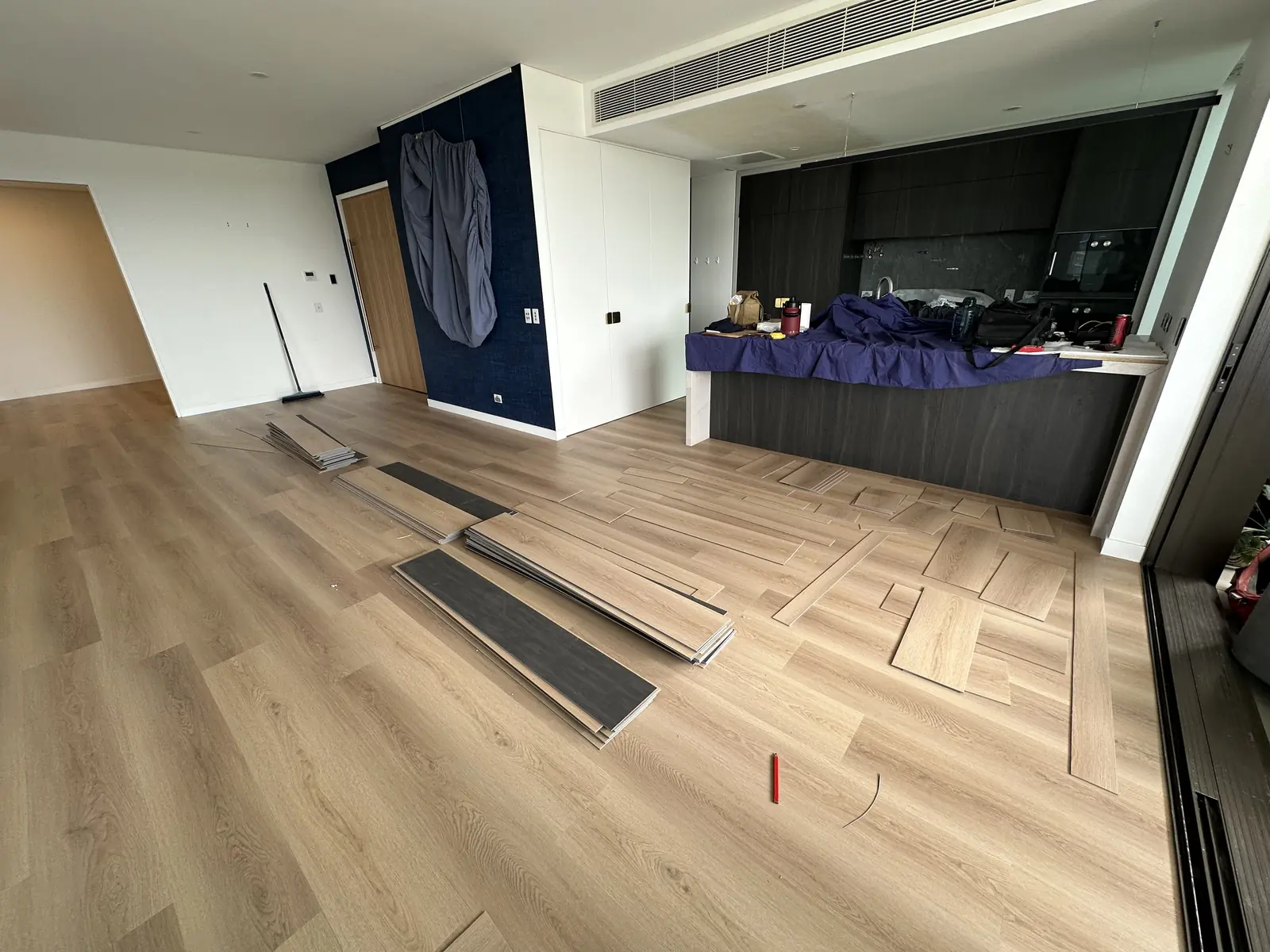 Plank flooring being installed through a Toowong apartment living area with the kitchen covered for protection